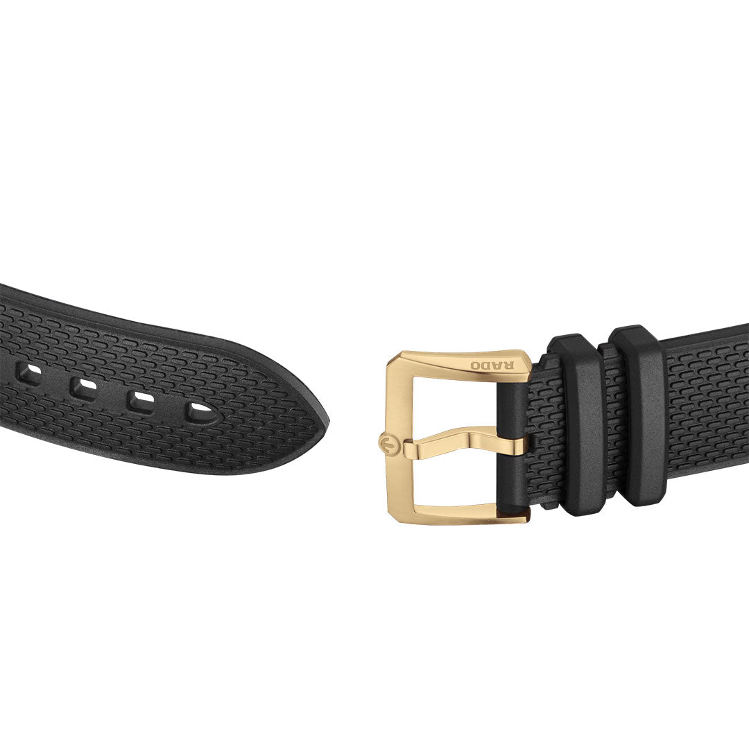 A black textured watch strap with a gold buckle engraved with “RADO,” inspired by the classic design of the RADO Captain Cook X European Cricket Special Edition Automatic 42mm Watch, is displayed against a white background.