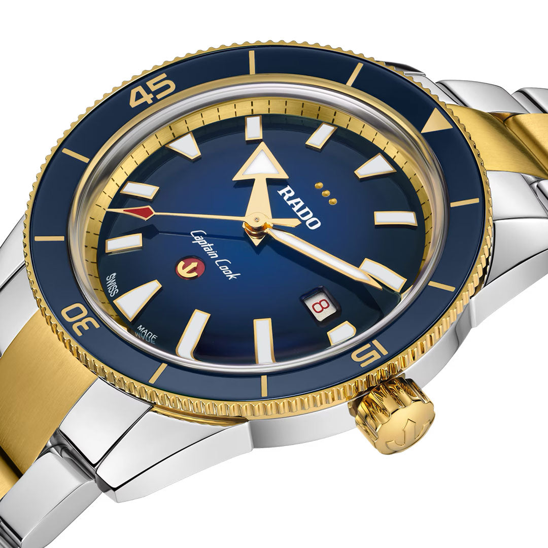 A close-up of the RADO Captain Cook X European Cricket Special Edition Automatic 42mm watch featuring a blue dial, gold bezel and accents, stainless steel band, automatic movement, and a date display at 3 o’clock.