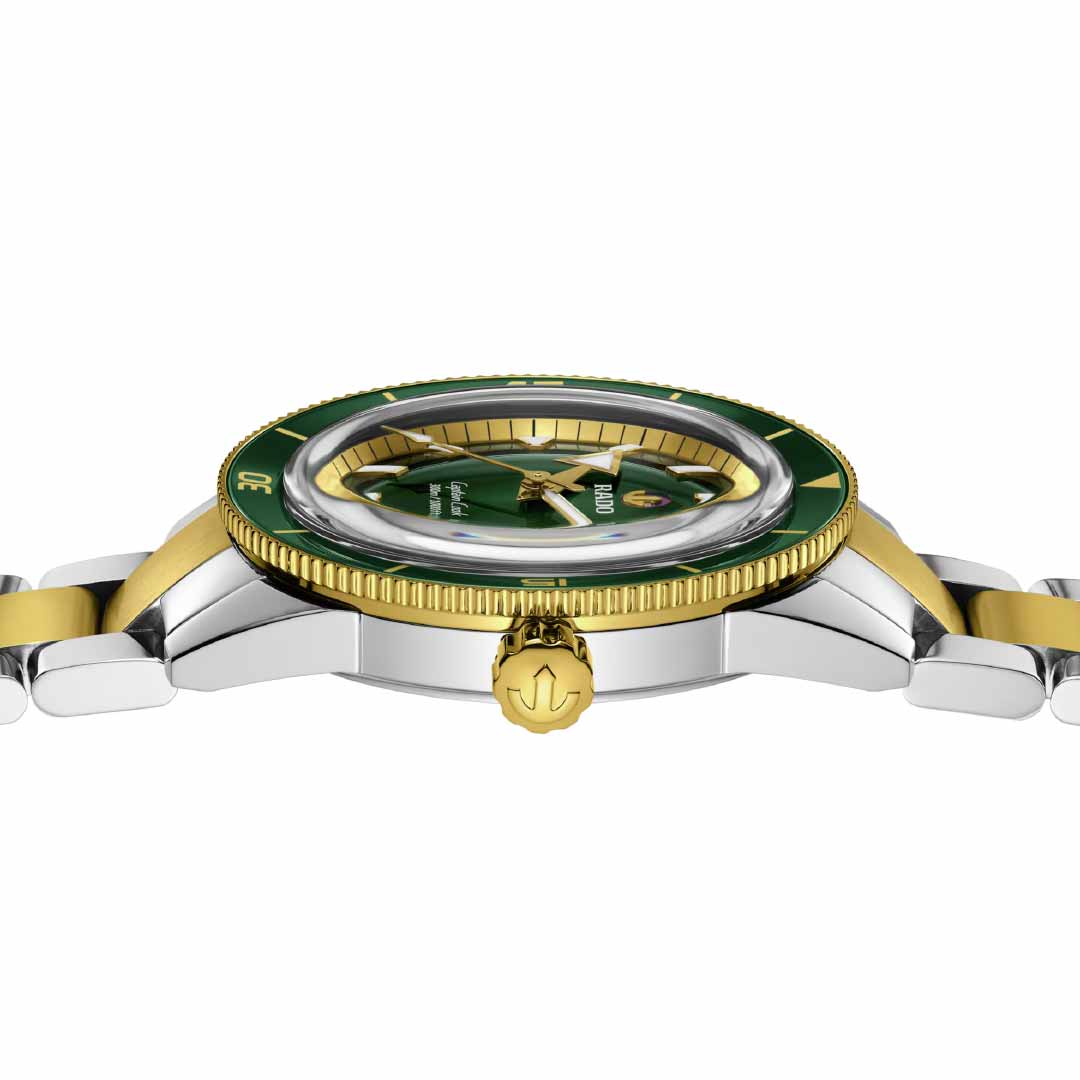 Side view of the RADO Captain Cook Automatic 42mm Watch showcasing its gold and silver band. This exquisite watch features a green dial and bezel, enhanced by a gold crown and anchor detail. Its intricate design emphasizes the Rado R763 automatic movement and precision craftsmanship in metallic tones.