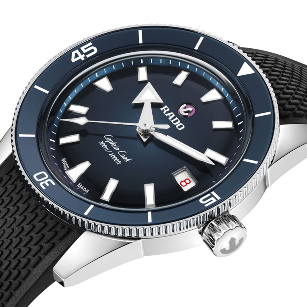 Close-up of the RADO Captain Cook Automatic 39mm Watch featuring a blue ceramic bezel, black textured strap, dark dial with bold white hour markers, date window at 3 o’clock, and prominent minute and hour hands.