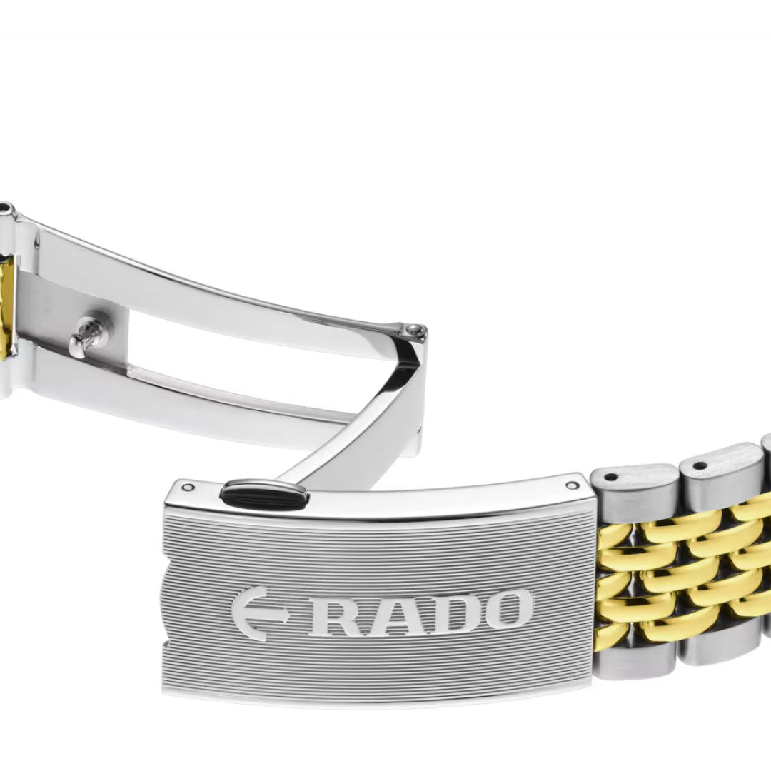 A close-up of the metal clasp engraved with "RADO" and logo, attached to a two-tone gold and silver link band from the Rado Captain Cook Automatic 39mm vintage dive watch.