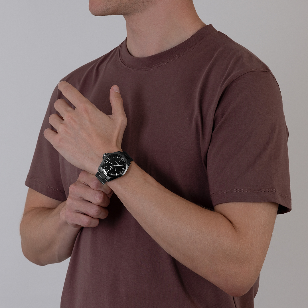A person wearing a black high-tech ceramic RADO Captain Cook Discover Automatic 40.7mm Watch with a dark metal link bracelet on their left wrist.