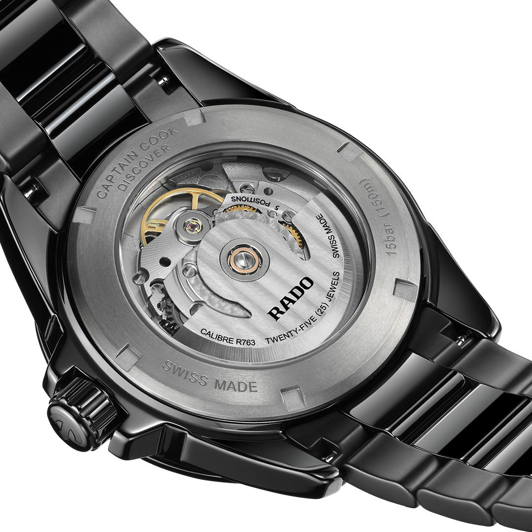 The black high-tech ceramic case of the RADO Captain Cook Discover Automatic 40.7mm Watch is flipped to show the transparent case back, revealing the intricate internal movement, gears, and markings of the automatic mechanism.