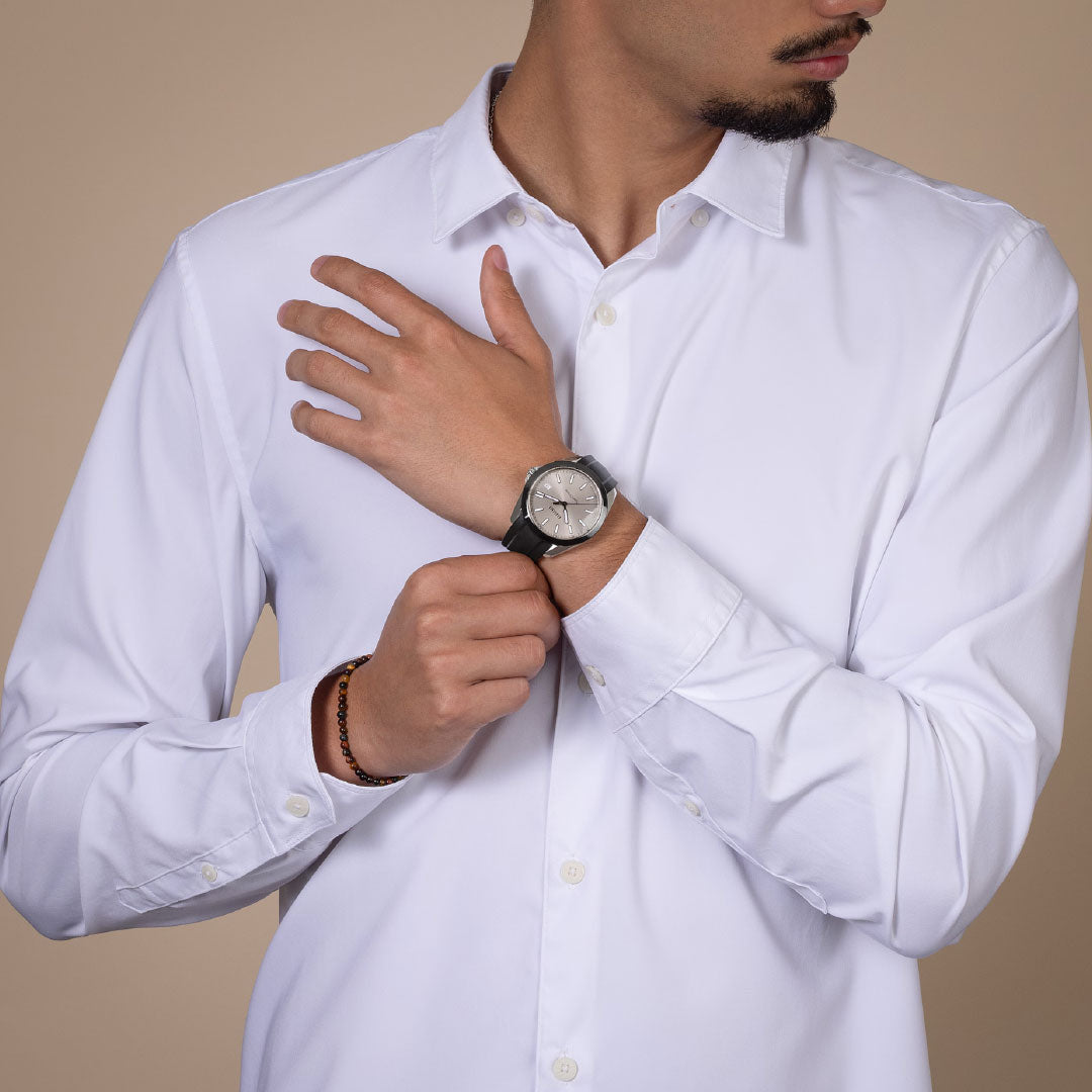 A man in a white button-up shirt models the RADO HyperChrome Quartz 41.5mm Watch with a high tech ceramic bezel on his left wrist, his right hand resting on his forearm, set against a plain beige background.
