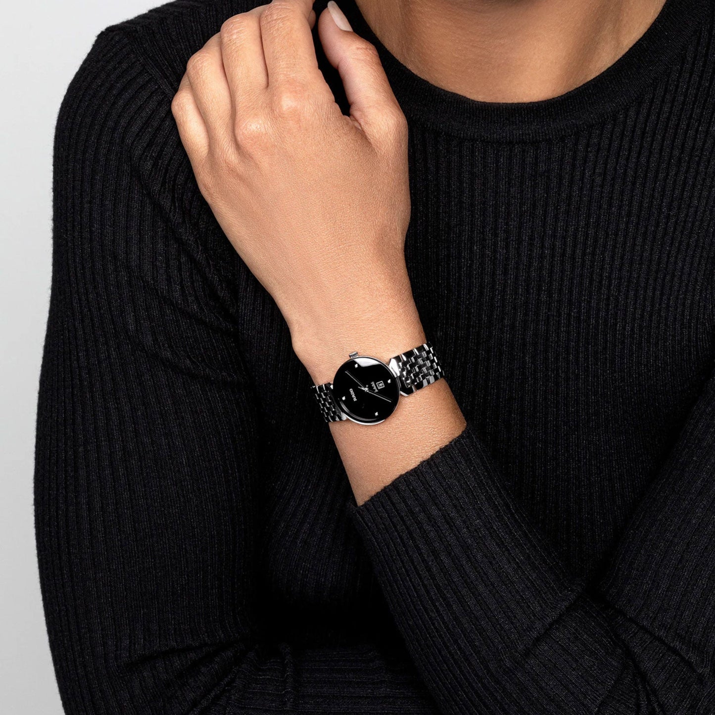 A person in a black long-sleeve sweater displays a sophisticated RADO Florence Diamonds Quartz 30mm watch, Swiss-made with a silver chain strap. Their hand rests on their shoulder, emphasizing the elegance of the timepiece against their outfit. Neutral background.