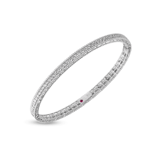 The Roberto Coin Symphony Princess 18K White Gold Diamond Bangle is a delicate piece with intricate designs, featuring a small red stone set into the band. Crafted with elegance, this bangle exemplifies Roberto Coin's attention to detail as it casts a subtle shadow against a plain, light background.