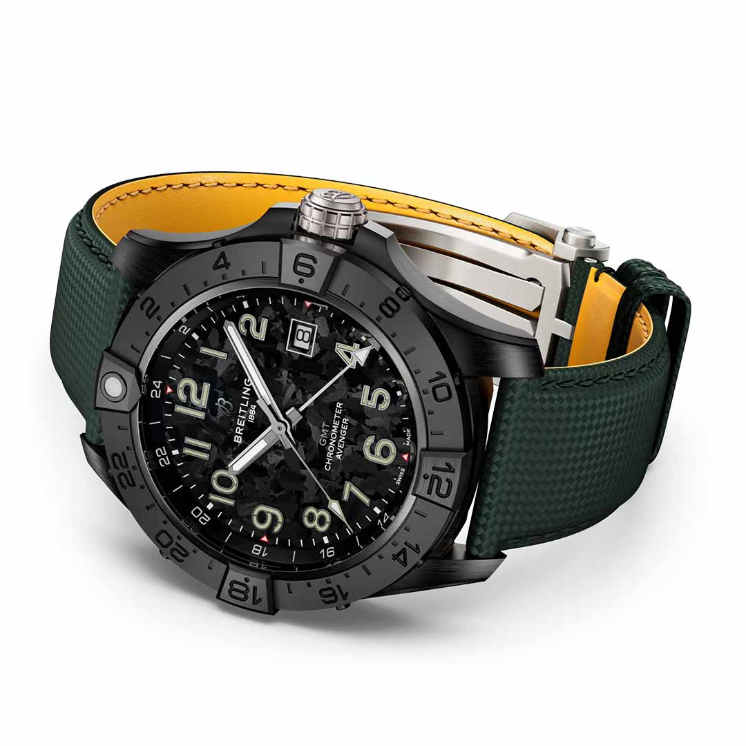 The BREITLING Avenger Automatic GMT 44 Night Mission is a black and green luxury wristwatch featuring a metallic bezel and luminescent numerals that exude an aviation style. Its face displays the Breitling brand name, along with the date and multiple hands, while boasting water resistance. The strap is crafted from green fabric with a bright yellow interior lining.