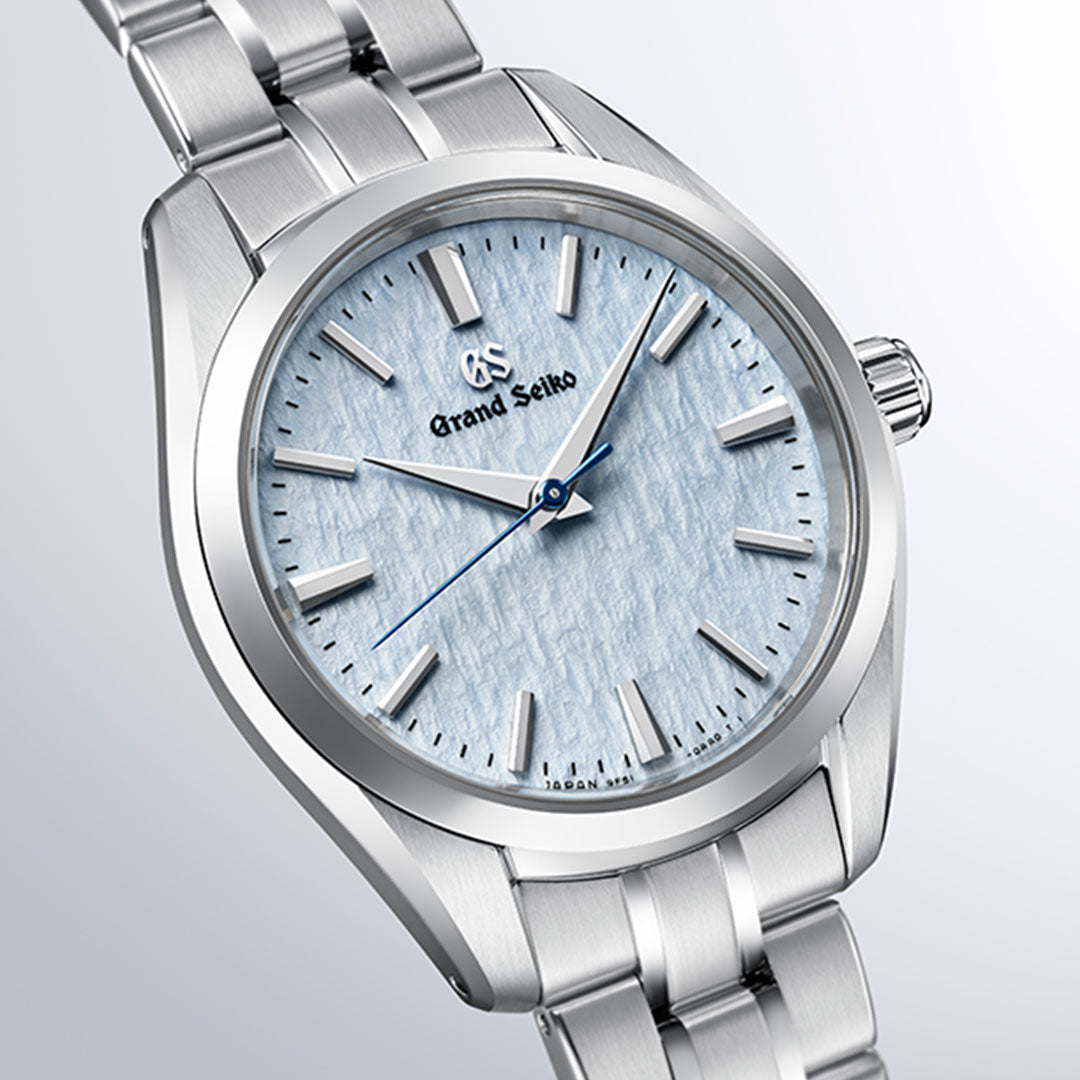 The Grand Seiko Heritage Collection 9F51 Quartz 33mm Watch features a textured light blue dial with silver hour markers, a sophisticated silver case and bracelet, and a distinctive blue second hand. Powered by Grand Seiko’s precise Caliber 9F51 movement, this elegant timepiece also has its crown set on the right side.