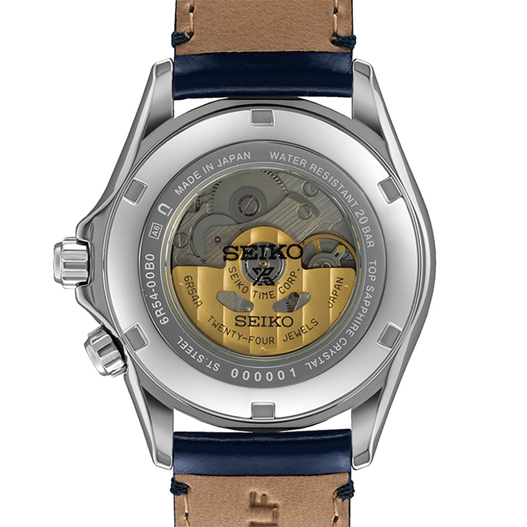 The image displays the reverse side of a Seiko Prospex Land Automatic With Manual Winding 39.5mm Watch, highlighting a transparent case that reveals the complex Caliber 6R54 mechanical GMT movement. Engraved text indicates it's crafted in Japan, water-resistant, and decorated with 24 jewels, completed by a leather strap.