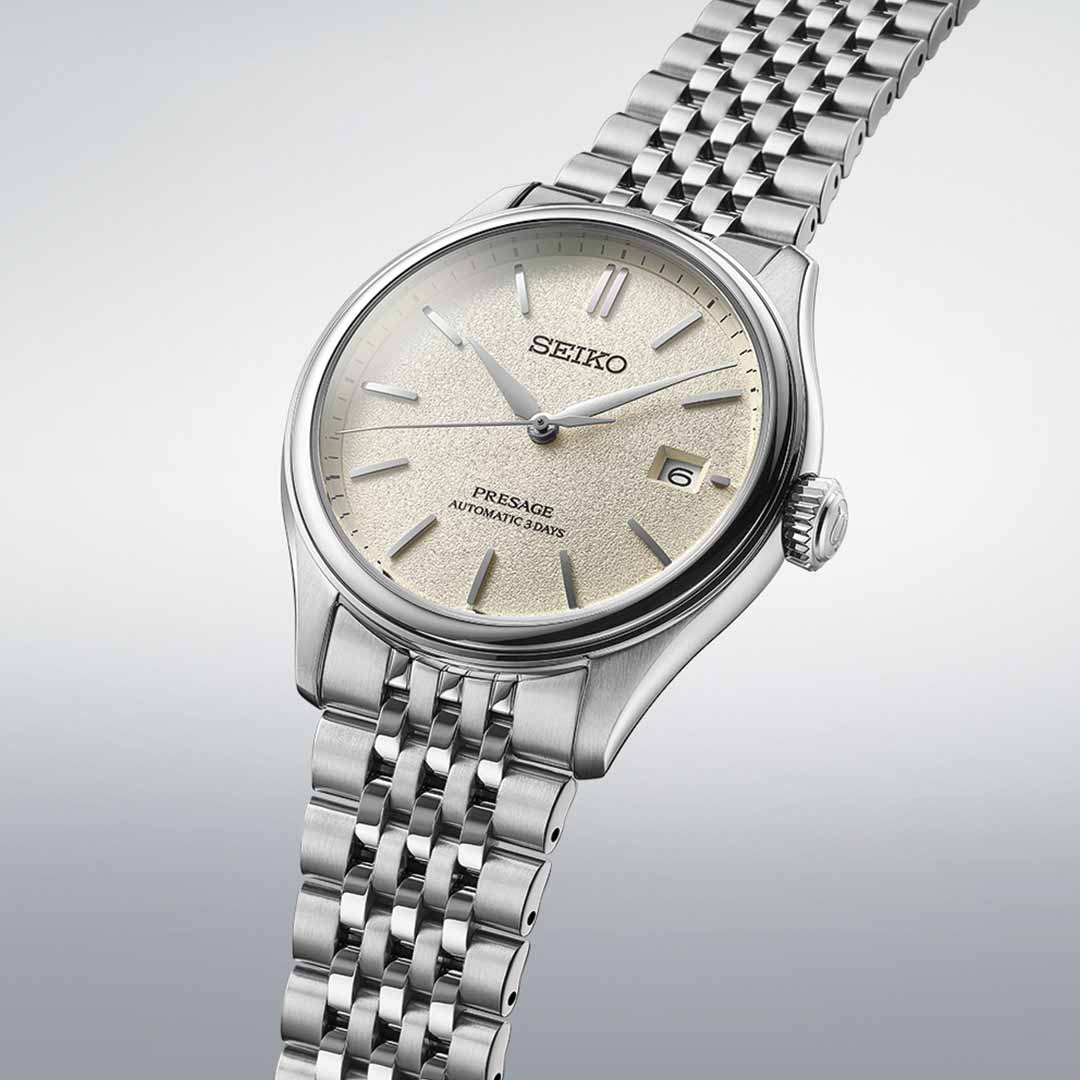 The Seiko Presage Classic Series Automatic with Manual Winding 40.2mm Watch exemplifies Japanese craftsmanship, boasting a silver automatic movement and a textured champagne-colored dial with a date function at three o'clock. Its stainless steel bracelet and minimalist hour markers add the finishing touches to this elegant timepiece by Seiko.