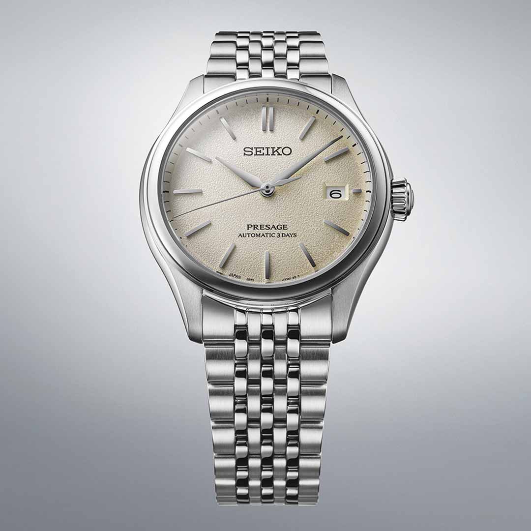 The Seiko Presage Classic Series Automatic with Manual Winding 40.2mm Watch from Seiko exemplifies Japanese craftsmanship with its textured beige dial and automatic movement. Its elegant design boasts slim silver hour markers and hands, along with a date display positioned at 3 o'clock, all set against a subtle light gradient background.