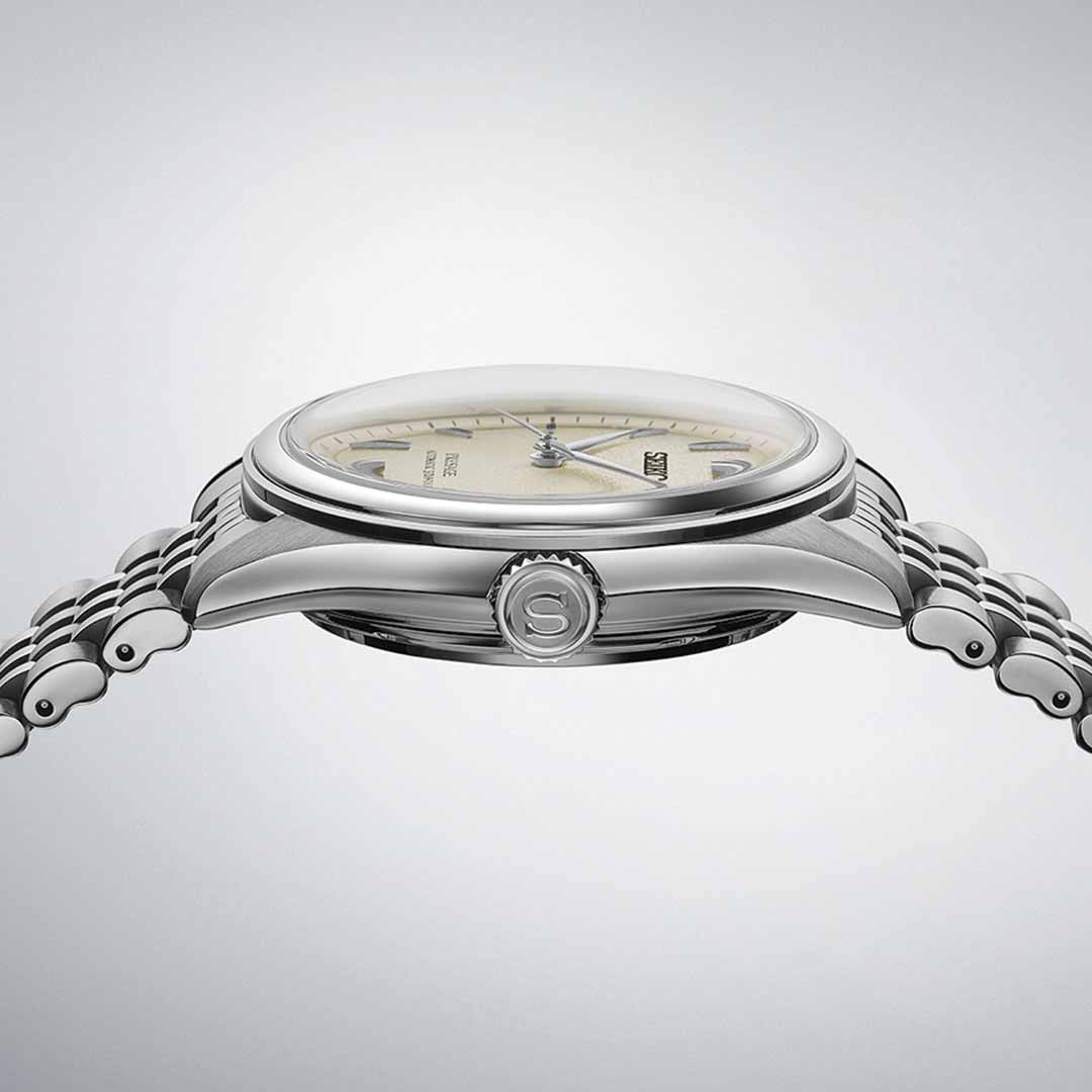 A side view of the elegant Seiko Presage Classic Series Automatic With Manual Winding 40.2mm Watch, featuring a sleek, polished bezel and a metallic bracelet. The watch exudes minimalist elegance with its intricate Japanese craftsmanship and cream-colored dial. The crown is embossed with an "S" logo.