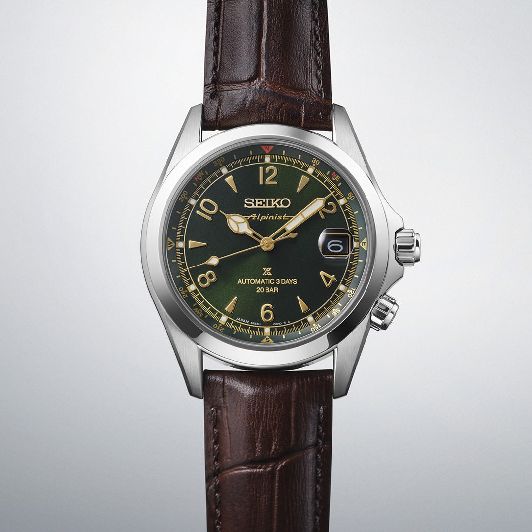 The Seiko Prospex Land Automatic With Manual Winding 39.5mm Watch by Seiko features a silver case, brown leather strap, striking green dial with gold markers, and a date display at the 3 o’clock position—all showcased against a light gray background. This automatic timepiece seamlessly combines rugged sophistication with timeless design.
