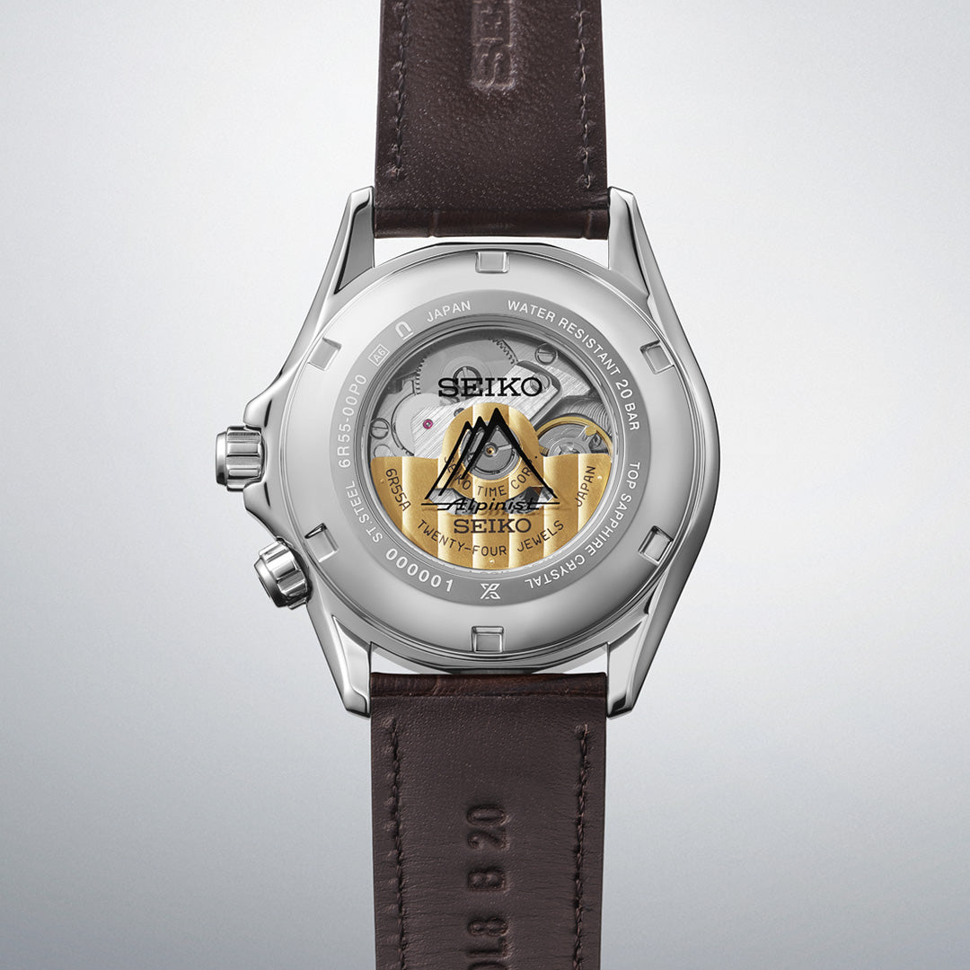 A Seiko Prospex Land Automatic With Manual Winding 39.5mm watch from Seiko is shown from the back, revealing its transparent caseback with visible movement components and gold accents. The brown leather strap and engraved elements enhance the refined automatic design, all housed in a classic 39.5mm case.