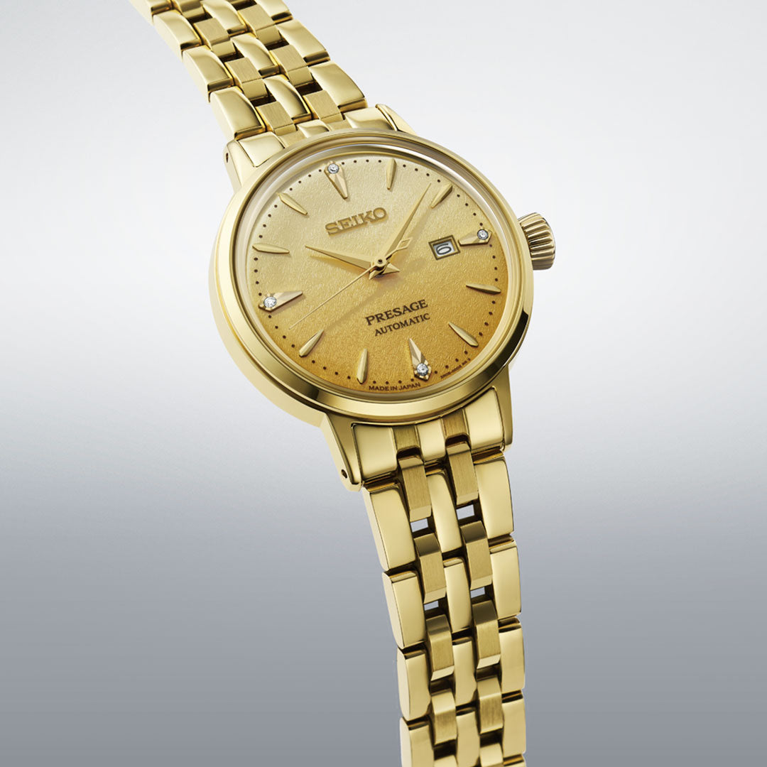 The Seiko Presage Cocktail Time Automatic with Manual Winding 30.3mm features a textured gold dial, gold hour markers and hands, date display, and a gold metal bracelet. Photographed against a light gradient background.