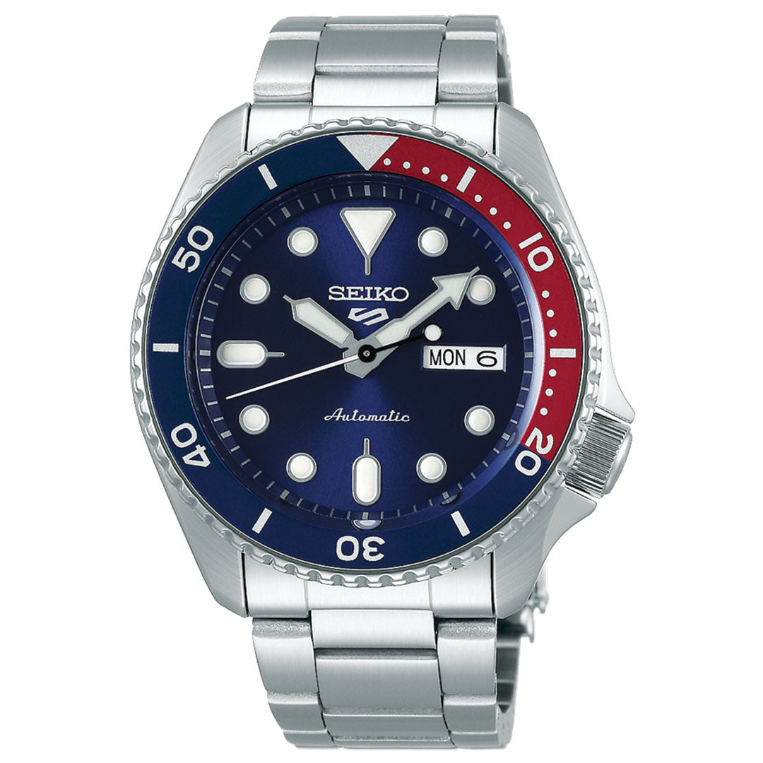 The Seiko 5 Sports SKX Series Automatic 42.5mm Watch by Seiko boasts a stainless steel case and band. Its blue dial is complemented by white markers and a bold red-blue bezel, elegantly showcasing the day and date at the 3 o'clock position.