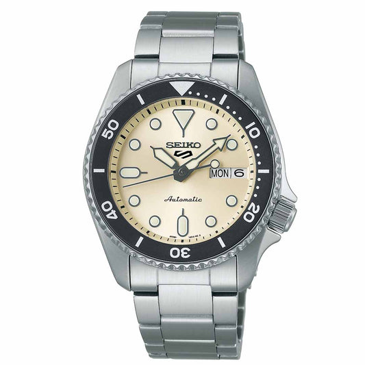 The Seiko 5 Sports SKX Series Automatic 38mm Watch by Seiko features a stainless steel band, a beige dial, and a black rotating bezel with white markings. Its luminous hour markers and hands display the time, complemented by the day and date function for added convenience.