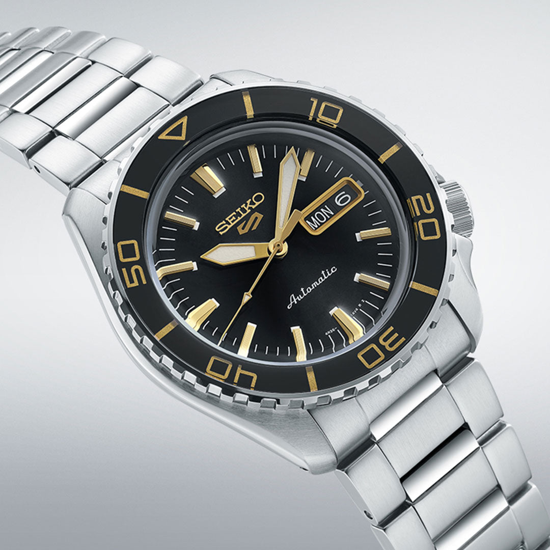Indulge in luxury with the Seiko 5 Sports SKX Series Automatic 42.5mm Watch by Seiko, showcasing a sleek black face and a stainless steel silver band. The elegant timepiece features gold and white markers that enhance the day and date display, paired with a rotating black bezel embellished with gold accents.