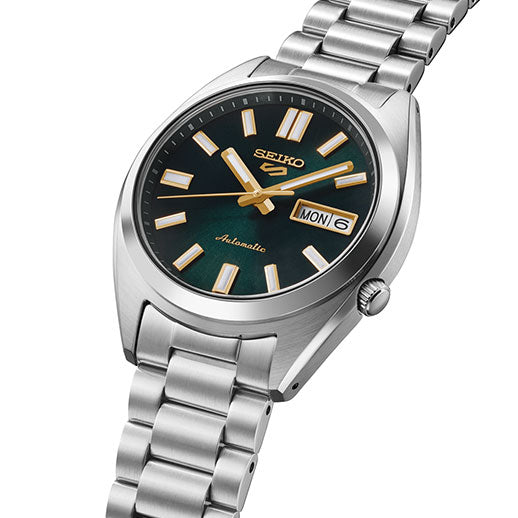 The Seiko 5 Sports SNXS Series Automatic with Manual Winding 37.4mm Watch features a silver case, green dial, gold hour markers and hands, day-date display showing "MON 6," metal link bracelet, and automatic movement label on the face.