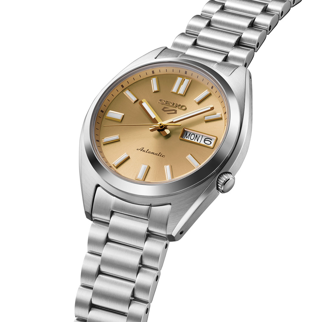 The Seiko 5 Sports SNXS Series Automatic 37.4mm Watch by Seiko features a stainless steel case and band, highlighted by a gold dial with silver hour markers and hands. This automatic timepiece includes both day and date displays at the 3 o’clock position, offering a blend of classic style and dependable functionality.
