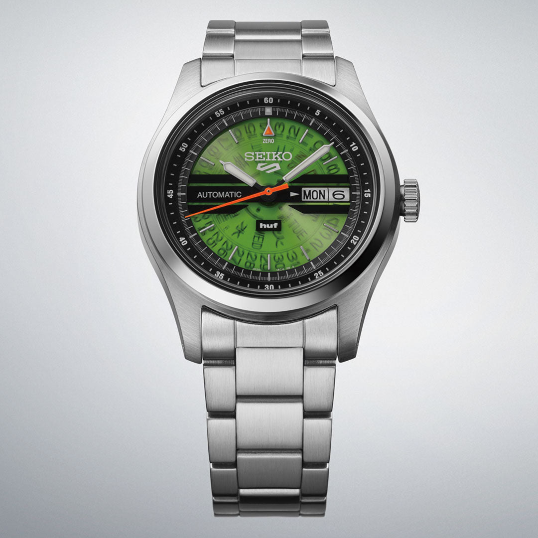 The Seiko 5 Field Series Automatic 39.4mm HUF Limited Edition (7,000 pieces) features a green dial with black outer ring, day/date display, luminous hands, and stainless steel bracelet, photographed on a light gray background.