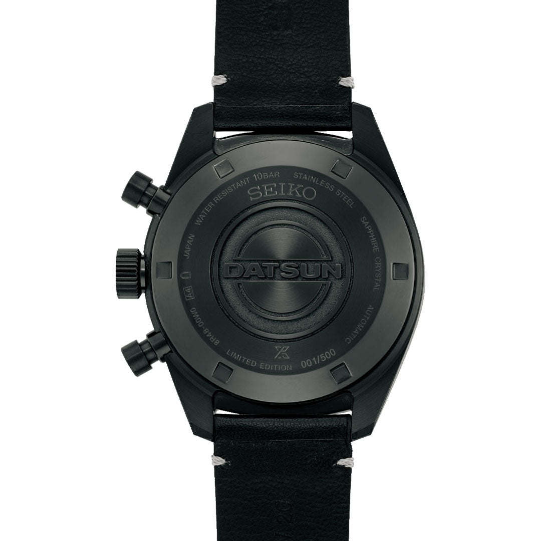 The back of a Seiko Prospex Speedtimer Datsun 240Z Chronograph shows the "DATSUN" engraving in the center, with "LIMITED EDITION 001/500" and other specs around the edge on its black case and leather strap.