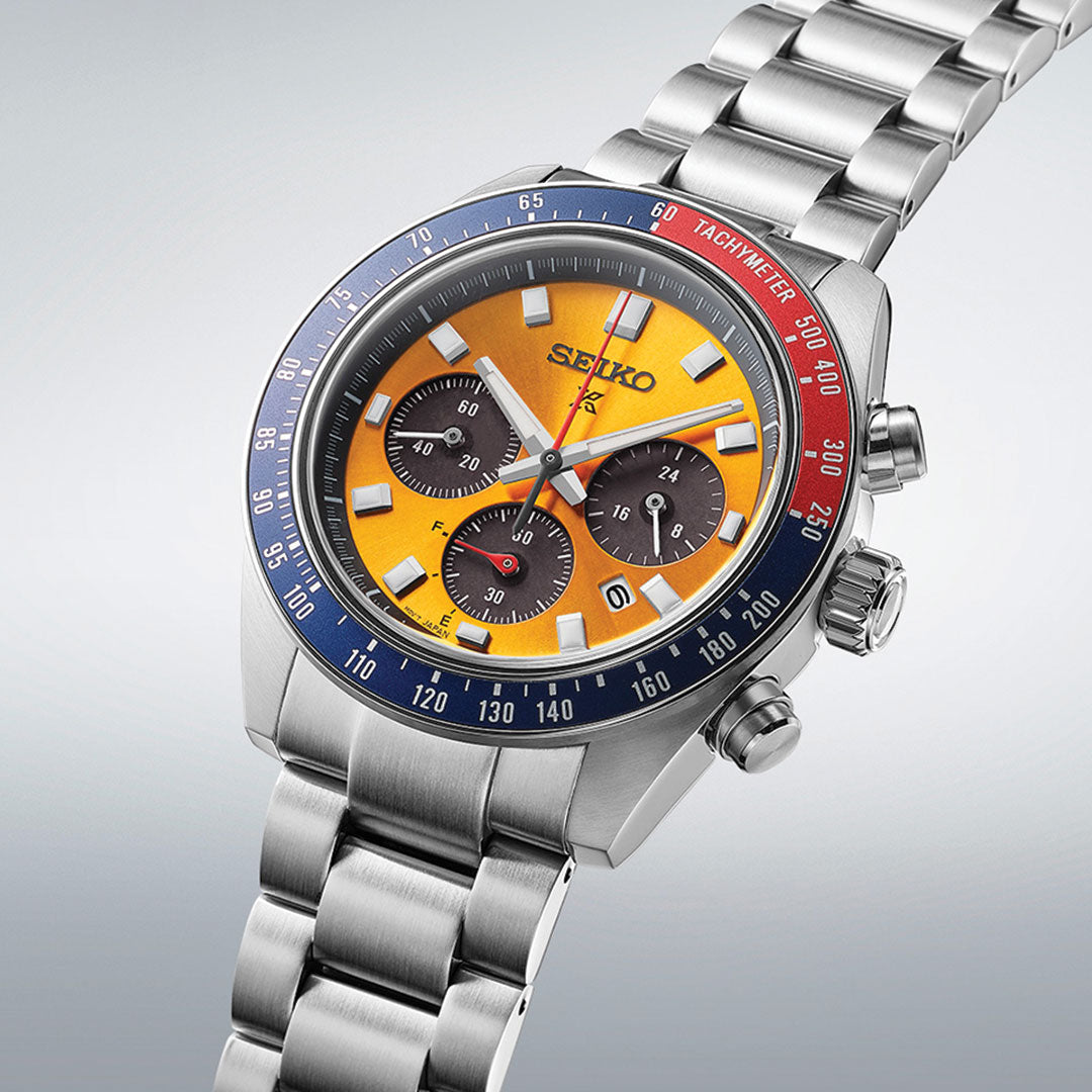 The Seiko Prospex Speedtimer Solar 41.4mm Watch by Seiko exhibits a robust design featuring a silver metal band. The vibrant yellow dial includes three sub-dials and is framed by a blue and red tachymeter bezel. This solar-powered timepiece captures the timeless elegance of a classic chronograph with its sleek silver accents.