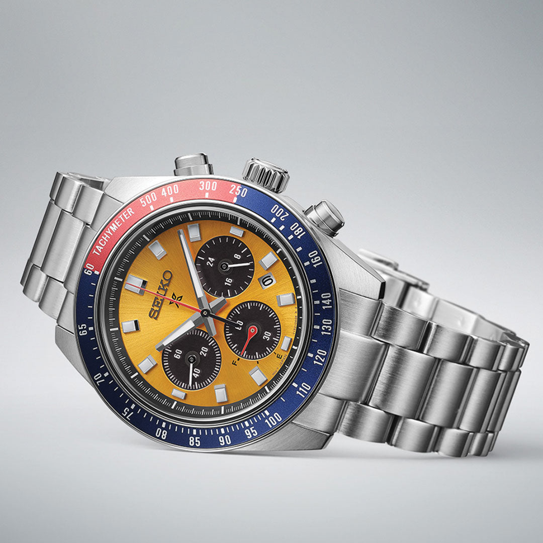 The Seiko Prospex Speedtimer Solar 41.4mm Watch is a durable design showcasing a silver stainless steel case. This solar-powered timepiece includes a yellow and black dial with three sub-dials and a date window. The blue bezel, accented with red, features a tachymeter scale, prominently displaying the Seiko brand name.