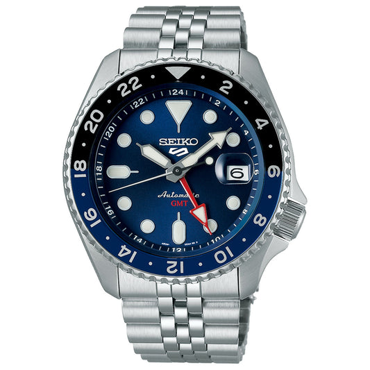 The Seiko 5 Sports SKX Automatic With Manual Winding 42.5mm Watch from Seiko features a silver metal band and an eye-catching blue and black bezel. It is equipped with Hardlex glass, showcasing a blue dial with prominent circular hour markers, a date display at the 3 o'clock position, and a red GMT hand for added functionality.