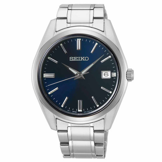 The Seiko Essentials Quartz 40.2mm Watch showcases a dark blue dial and durable sapphire crystal. Its design includes silver hour markers, a date window located at 3 o'clock, and the renowned "Seiko" brand positioned near 12 o'clock, all nicely complemented by a sleek metal link band.