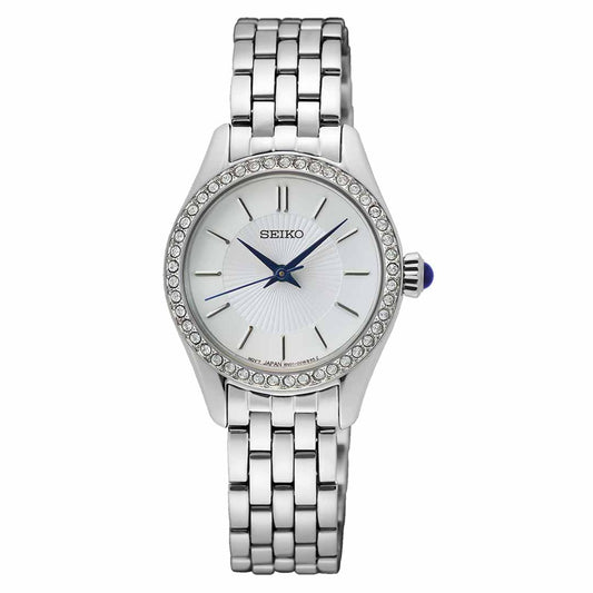 Introducing the Seiko Essentials Quartz 26mm Watch, a stunning piece by Seiko for women. This stainless steel watch features a round white dial adorned with silver hour markers and a striking blue second hand. Its bezel sparkles with small crystals, perfectly matched by an elegant silver link bracelet.