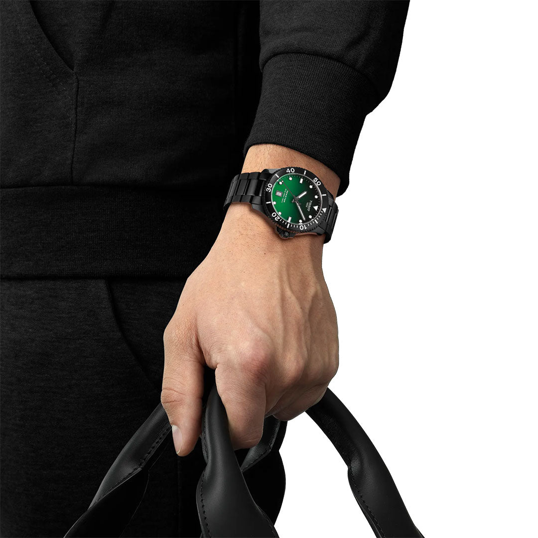 A person in black holds black handles and wears a Tissot Seastar 1000 Quartz 40mm watch, featuring a green and black face that epitomizes Swiss precision. The background is white.