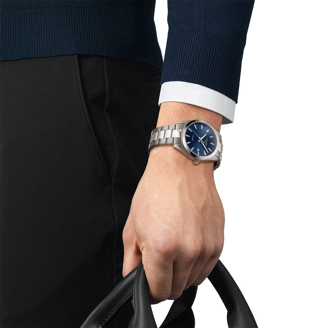 A person wearing a Tissot Gentleman Titanium Quartz 40mm Watch with a blue dial holds a black handle, dressed in a navy sweater and black pants.