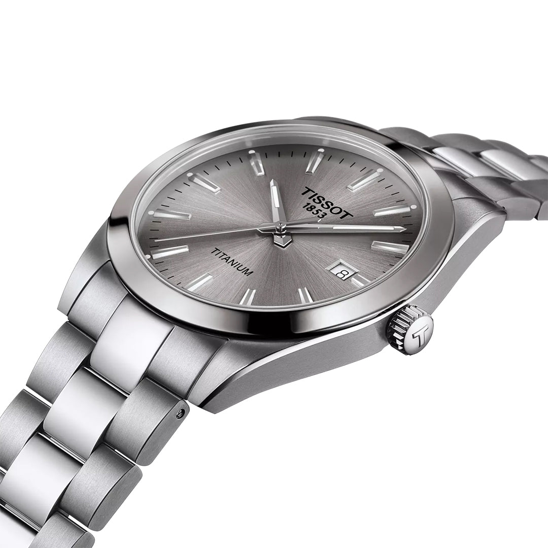 A close-up of the Tissot Gentleman Titanium Quartz 40mm Watch shows its titanium case, silver metal band, grey dial with silver hour markers, date display, and "Tissot 1853" and "Titanium" on the face.