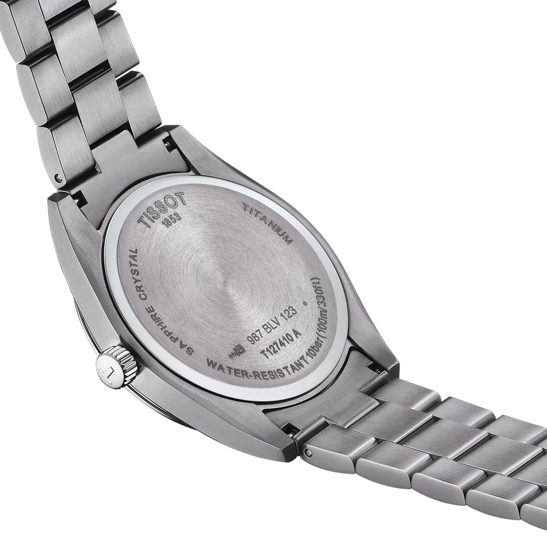 The image shows the back of a Tissot Gentleman Titanium Quartz 40mm Watch with a silver metal bracelet. The titanium case back is engraved with "TISSOT," "Titanium," "Sapphire Crystal," and "Water-Resistant 10 Bar (100m/330ft).