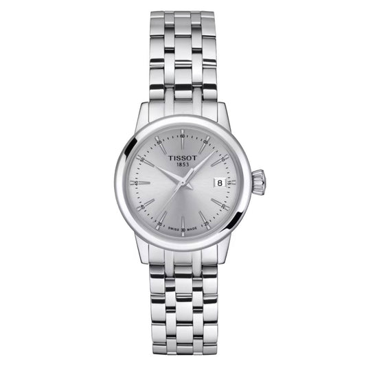 The Tissot Classic Dream Lady Quartz 28mm Watch is a stunning wristwatch with a 316L stainless steel case and a silver bracelet. It features a round face protected by scratch-resistant sapphire crystal, showcasing a silver dial with elegant hour markers and a date window at the 3 o'clock position. Its precise timekeeping is maintained by Swiss Quartz Movement, with "1853" elegantly displayed on the dial.