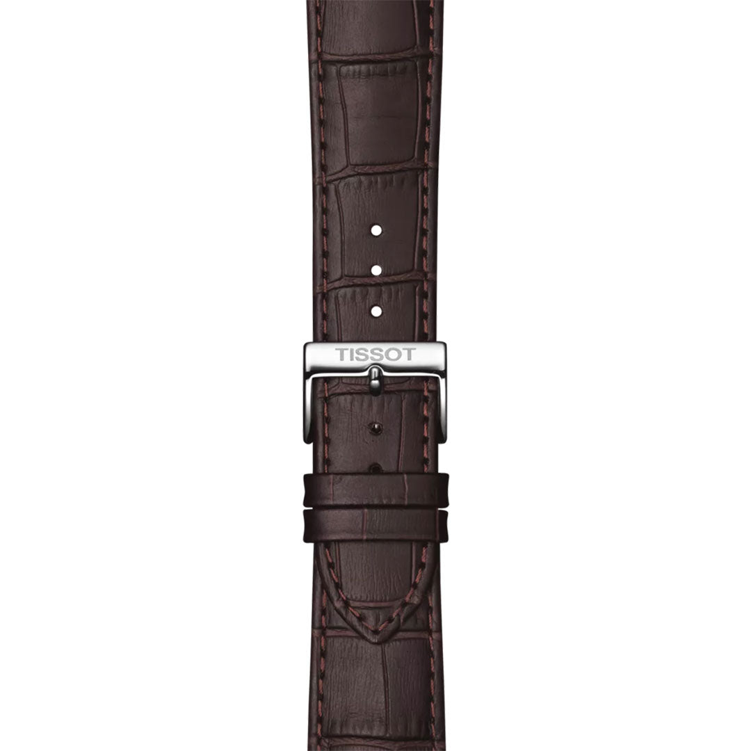 The Tissot Classic Dream Quartz 42mm watch features a brown leather strap with visible stitching and a silver Tissot-engraved buckle, adding sophistication to this classic timepiece, shown elegantly on a white background.