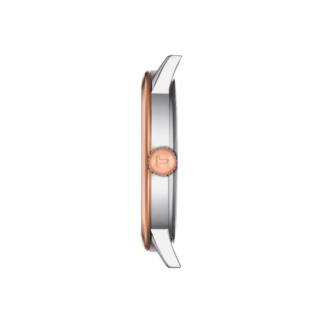 Side view of the Tissot Classic Dream Quartz 42mm Watch case showcasing its sophisticated two-tone design. The stainless steel case is elegantly finished with rose gold PVD and silver, featuring a crown with an engraved "T" logo on the side. This watch offers a sleek, minimalist profile and is powered by precise Swiss Quartz movement.