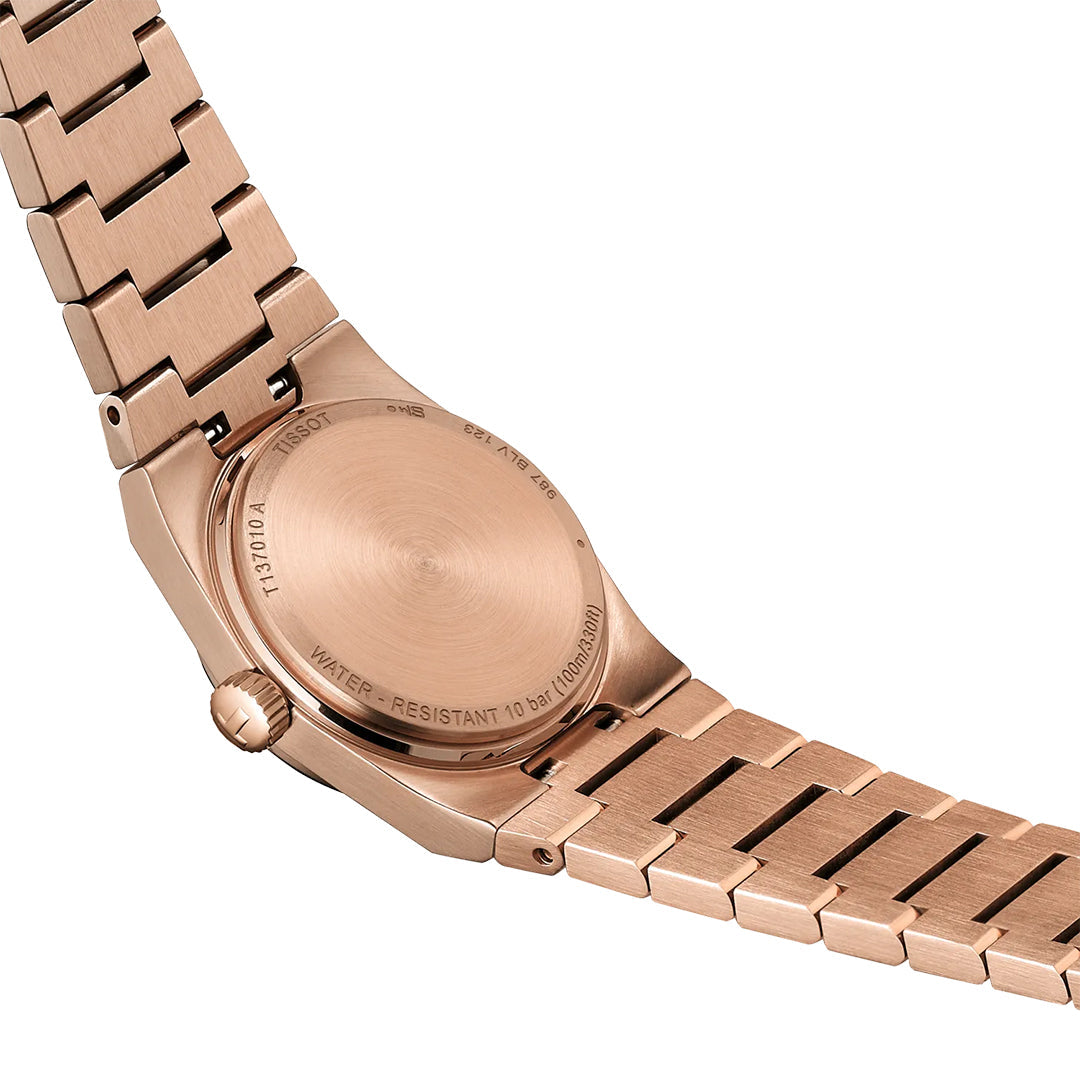 A close-up of the Tissot PRX Quartz 25mm Watch's rose gold metal link band and stainless steel case back, revealing engraved details, brushed finish, water resistance, quartz movement, and other specs from Swiss brand Tissot.