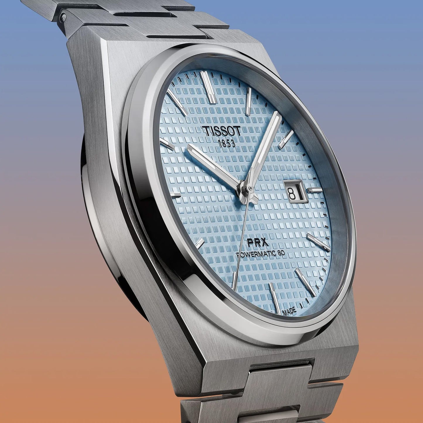 The Tissot PRX Quartz 35mm watch offers a light blue textured dial with retro silver hour markers and hands, a date display, and an elegant stainless steel integrated bracelet against a striking blue-to-orange gradient backdrop.