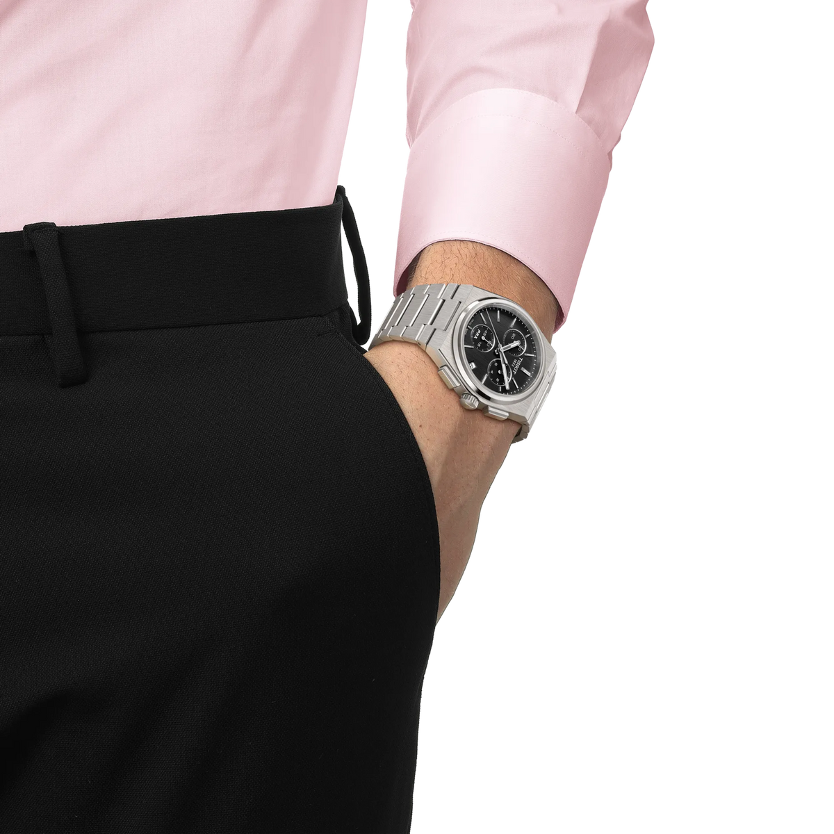 A person wearing a silver Tissot PRX Chronograph Quartz 41mm Watch with a black dial on their left wrist, their hand tucked into a black trouser pocket.