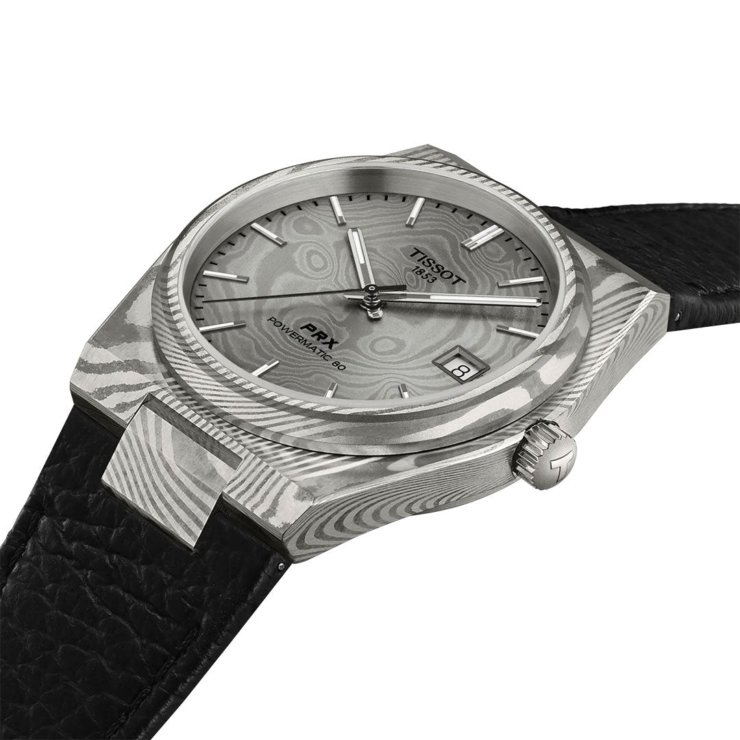 The Tissot PRX Damascus Steel Powermatic 80 Automatic 38mm Watch features a wave-patterned Damascus steel case, black leather strap, textured gray dial, silver hour markers, and a date window at 3 o'clock.