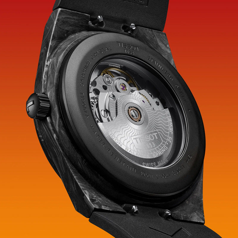 Close-up of the Tissot PRX Carbon Powermatic 80 Automatic 40mm watch, featuring a forged carbon case and a visible mechanical movement. The watch is displayed against a vibrant orange gradient background, highlighting its intricate gears and components beneath the sapphire crystal, showcasing Swiss craftsmanship by Tissot.