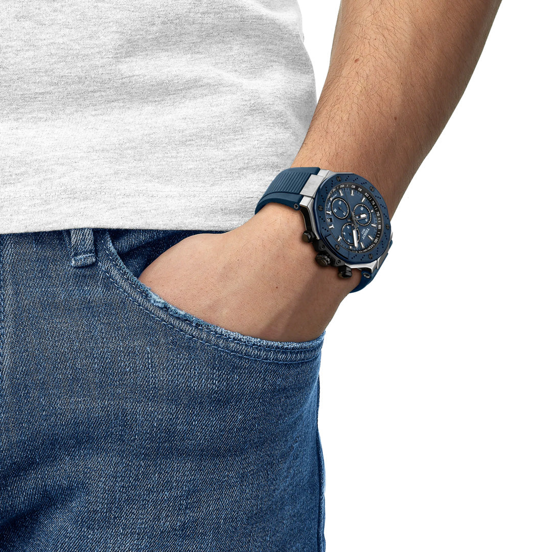 A person in a white t-shirt and blue jeans has their left hand in their pocket, showing off a striking Tissot T-Race Chronograph Quartz 45mm Watch with a bold, detailed face.
