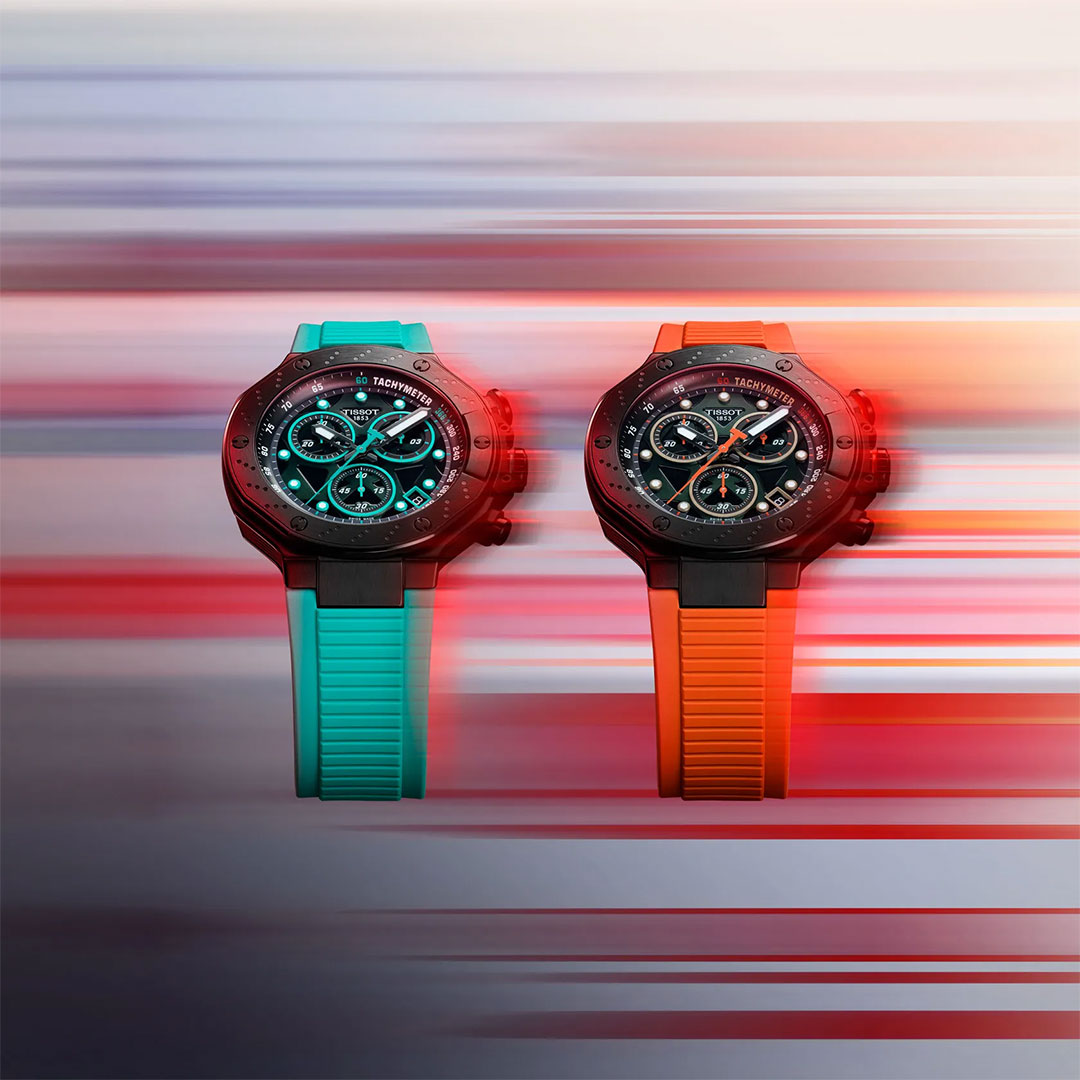 Two Tissot T-Race Chronograph Quartz 45mm watches with black dials—one with a blue strap, the other with orange—are displayed side by side against a dynamic, racing bike-inspired backdrop featuring vibrant blue and red lighting.