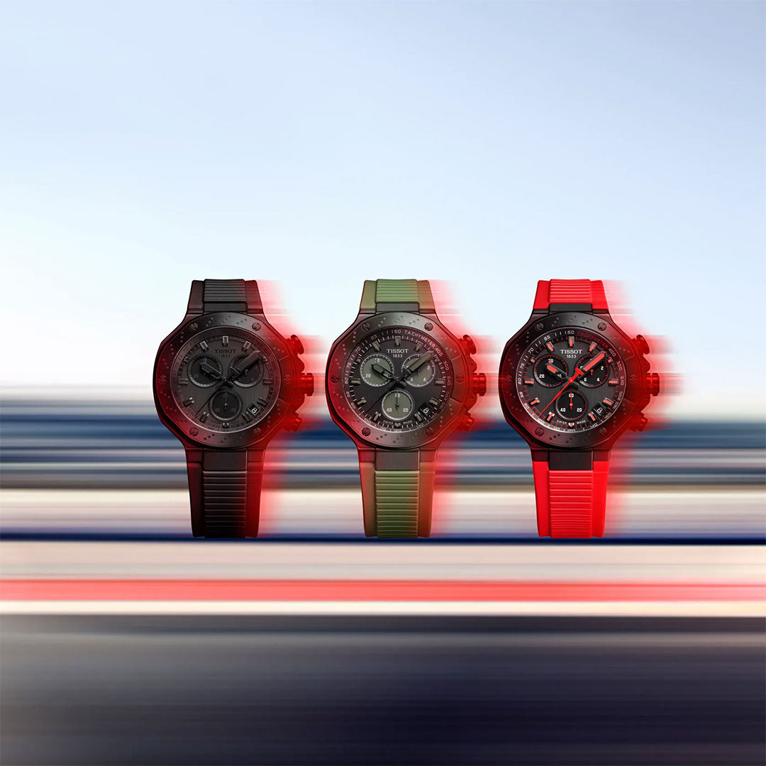 Three Tissot T-Race Chronograph Quartz 45mm Watches with black, green, and red straps are displayed side by side against a blurred background, emphasizing their stainless steel cases and sporty vibe.