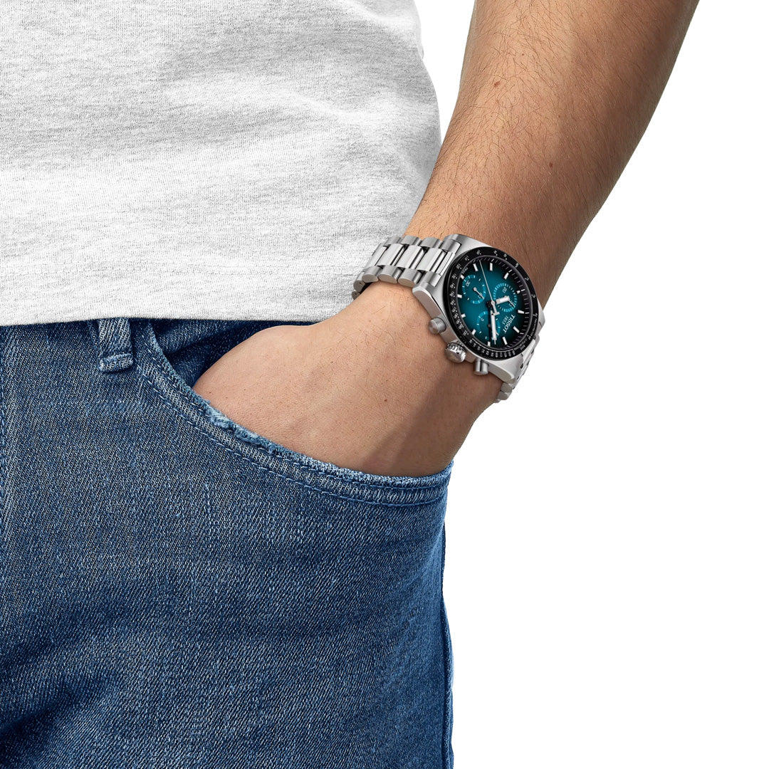 A person dressed in a white t-shirt and blue jeans, with their hand casually tucked into their pocket, wears a Tissot PR516 Chronograph Quartz 40mm Watch from Tissot featuring a blue dial.