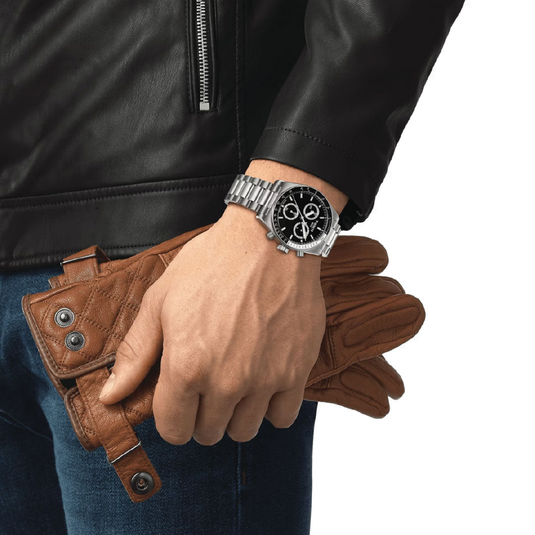 A person wearing a black leather jacket and a Tissot PR516 Chronograph Quartz 40mm Watch holds a pair of brown quilted leather gloves.