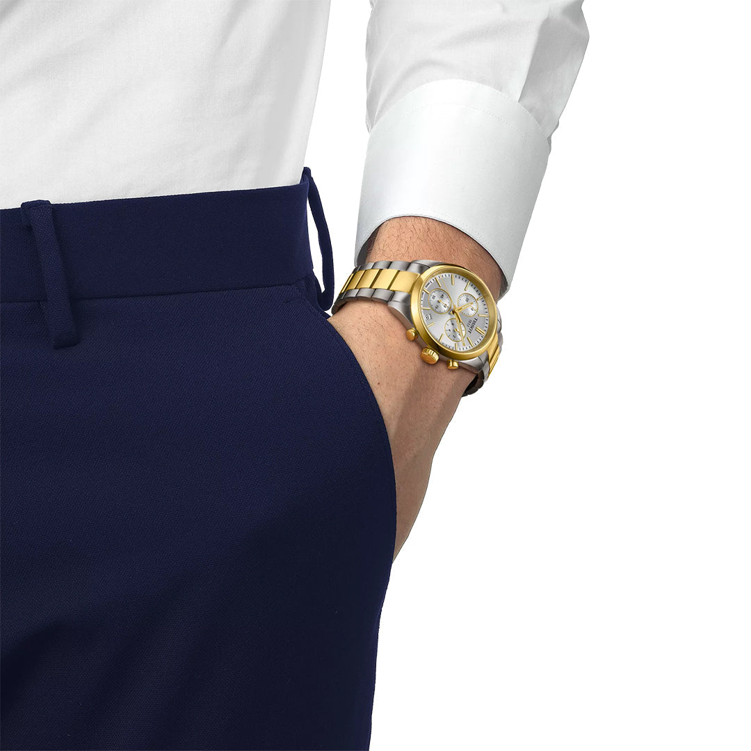 A person in a white dress shirt and navy blue pants has their hand in their pocket, showcasing the Tissot PR 100 Chronograph Quartz 40mm Watch, a stylish two-tone Tissot wristwatch designed for everyday durability.