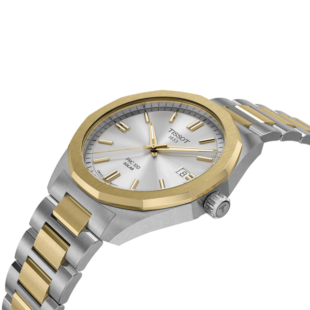 The Tissot PRC 100 Solar Quartz 39mm Watch features a round silver dial, gold bezel, gold markers and hands, date window at 3 o’clock, two-tone metal bracelet, and a crown with the “T” logo.